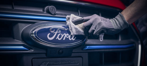 En hand som rengör ett Ford emblem på fronten av en Ford